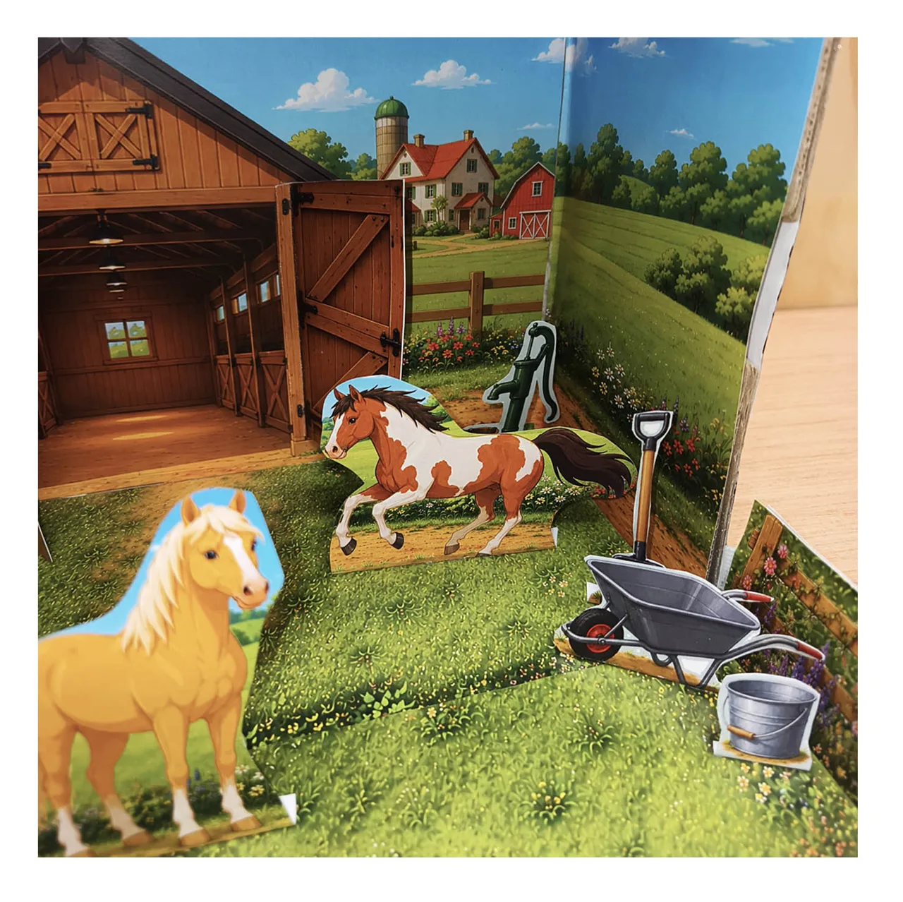 Close-up of the finished horse stable diorama with paper horses, flower-covered paddock fence and layered country background